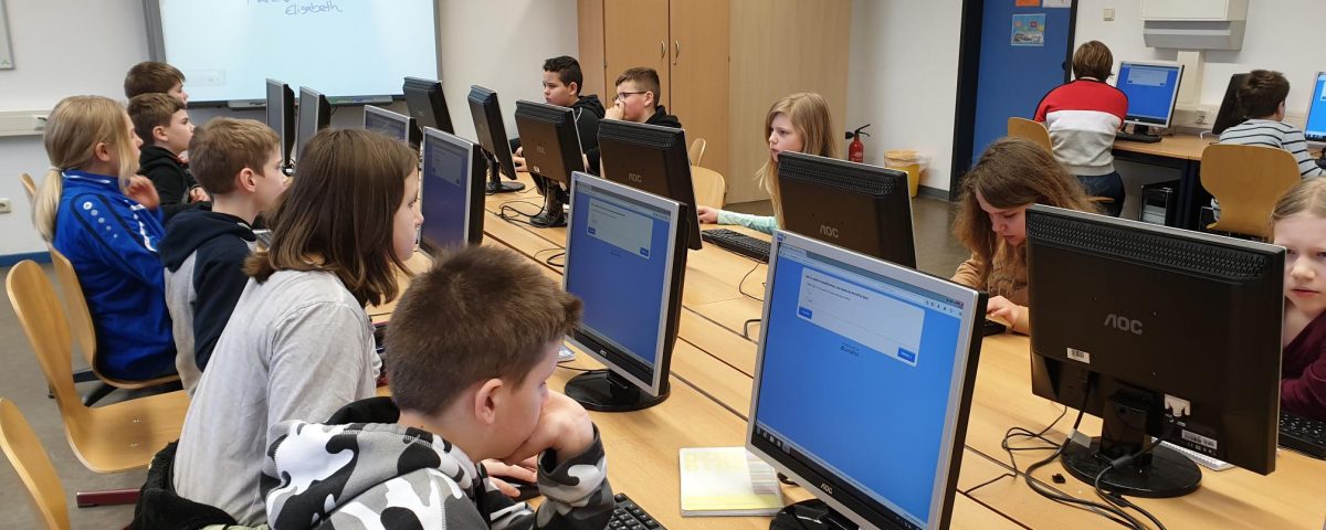 Mehrere Schüler sitzen an Computern und füllen einen online Fragebogen aus