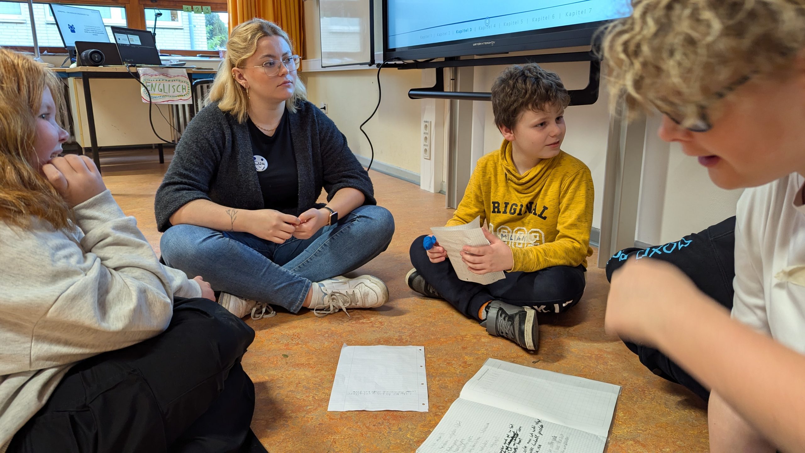 Eine junge Social Visionary sitzt mit drei weiteren Schüler:innen im Gespräch in einem Sitzkreis auf dem Boden.